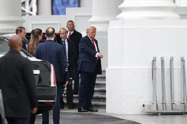 Image shows President Donald Trump pointing to a White House column. 
