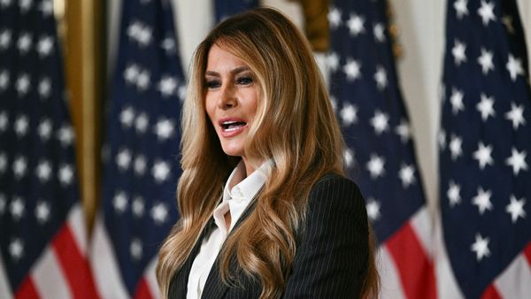 First Lady Melania Trump speaks in front of a backdrop featuring American flags.
