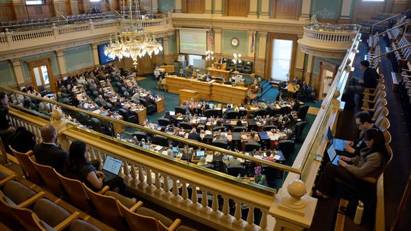 The view of the Colorado House chamber from the gallery up above, showing rows of desks with legislators sitting in chairs. 