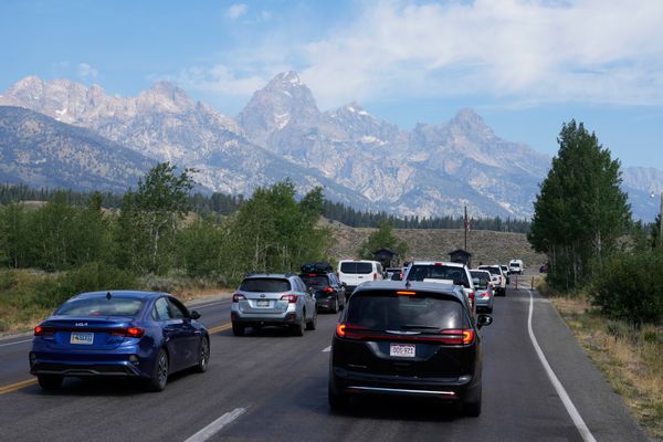 A small traffic jam on a very scenic road in Wyoming's Grand Teton National Park. The background is full of grey, craggy mountains that give way to pine trees and scrubby hills.