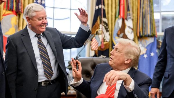 Lindsey Graham stands while talking to Trump, who is sitting down. Both men appear to be happy. 