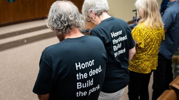 Attendees wearing shirts that read, "Honor the deed. Build the park," bow their heads in prayer during the invocation of the Taylor City Council Meeting, July 9, 2026.