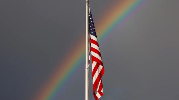 An American flag is shown in front of a rainbow.