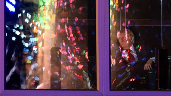 Through a window, U.S. President Donald Trump watches a fireworks display, which is reflected back toward the viewer because of the window. 