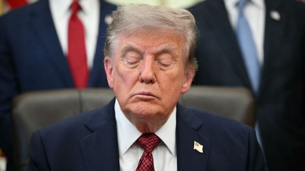 President Donald Trump, an older white man, wears a suit and sits in a leather chair with his eyes closed.