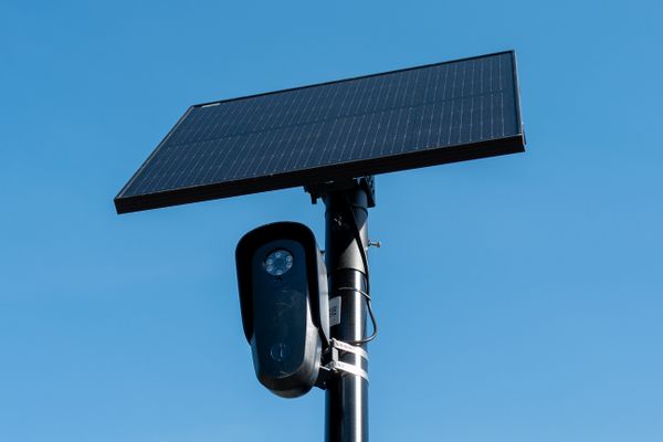 Flock license plate reader and camera with solar panel against a blue sky.