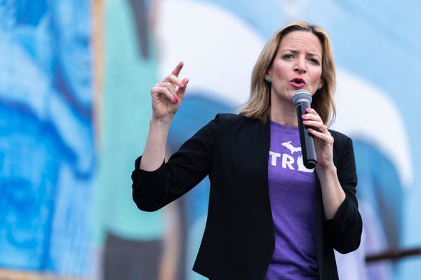 Michigan Secretary of State and gubernatorial candidate Jocelyn Benson, a blonde, middle-aged woman in a black suit and purple T-shirt, speaks into a microphone.