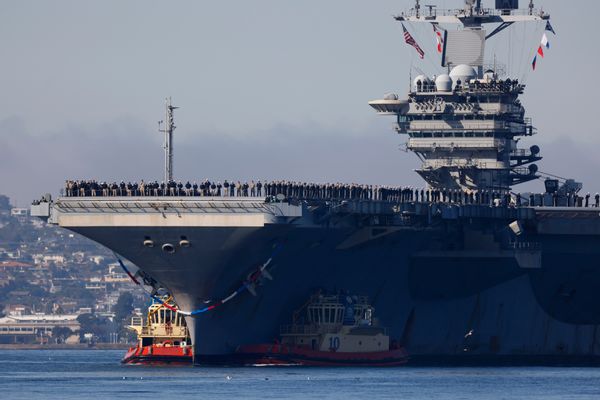 A large Naval aircraft carrier, the USS Abraham Lincoln, in the ocean with numerous Navy personnel on board. 