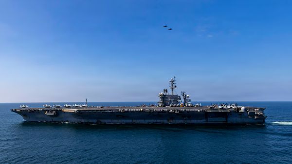 A large aircraft carrier ship on the water amid clear skies. 