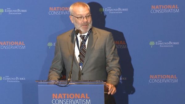 Heritage Foundation's Scott Yenor standing at a podium in a suit.