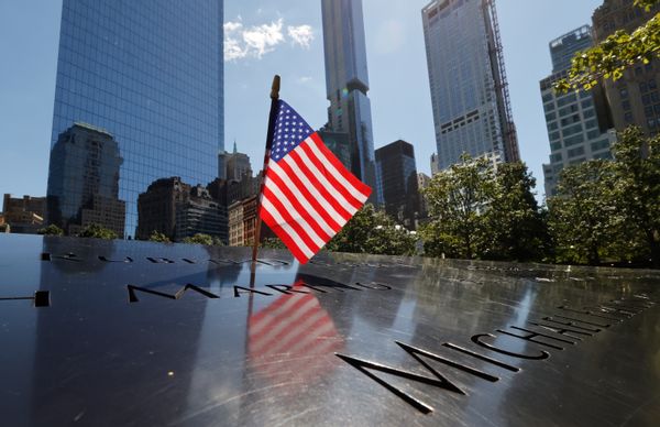 An American flag standing on a stone 9/11 memorial on a clear day in New York City. 