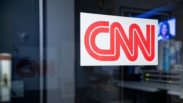 A zoomed-in photo of the CNN logo on a glass wall of CNN's booth in the White House press area. The lights are off in the booth; the photo was taken after Trump banned CNN journalists from the White House.