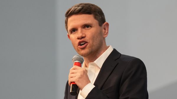 James Talarico, a youthful-looking white man, wears a black suit while talking into a handheld microphone.