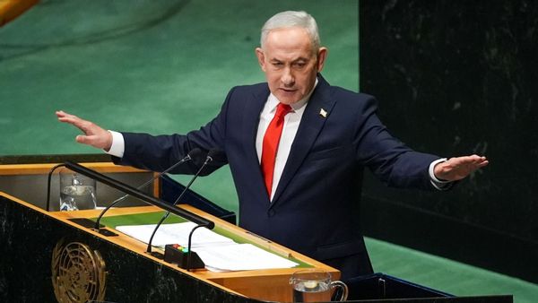 Image shows Israeli Prime Minister Netanyahu speaking while standing with his arms spread wide behind a podium at the United Nations General Assembly.