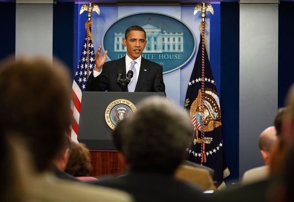 Then-President Barack Obama, a Black man, stands behind a lectern and speaks at a White House press briefing.
