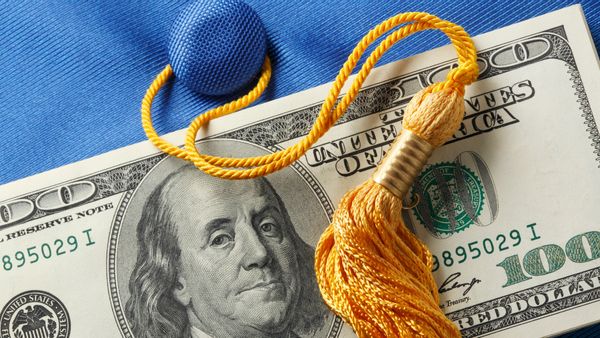 A U.S. hundred dollar bill laid on top of a blue graduation cap with a gold tassel. 