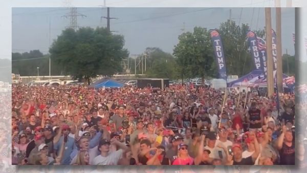 Image shows screenshot of a 2024 Trump rally with Trump 2024 flags in the background.