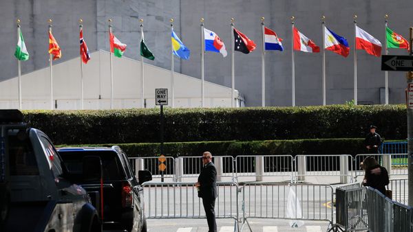Flags from different countries in a line outside of a large grey building. 