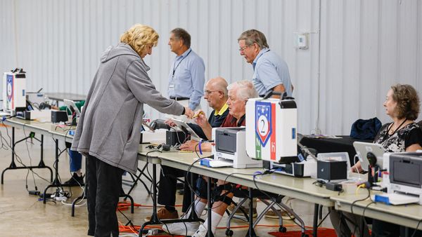 A woman with blonde hair and a gray coat vasts her vote at a polling place.
